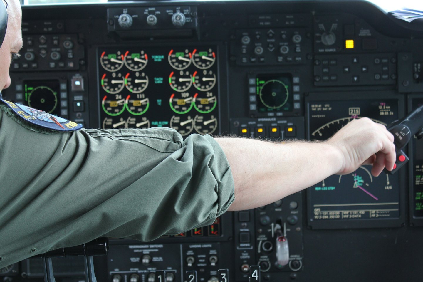 Pilot's hand controlling aircraft in busy cockpit.